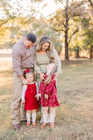 Family of four posing together outdoors with young children in red outfits during sunset.