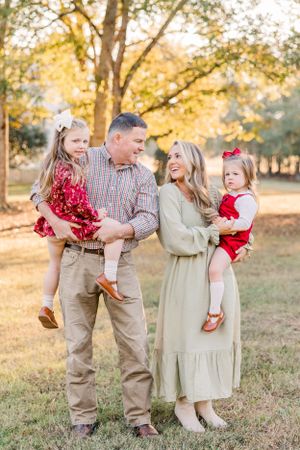 Family portrait in park with two young daughters wearing red and khaki outfits.