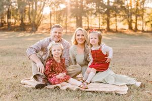 Family sitting on blanket in field during golden hour photo session.