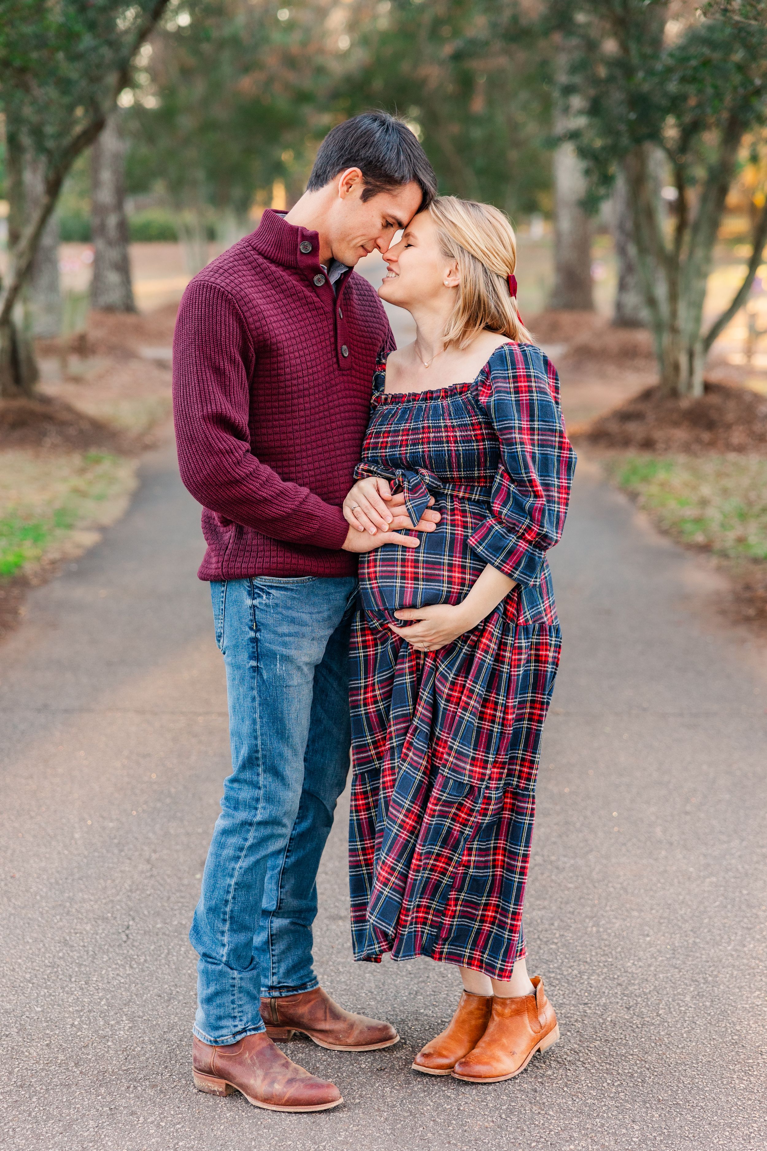 Intimate moment between expecting couple on tree-lined path during maternity photoshoot.