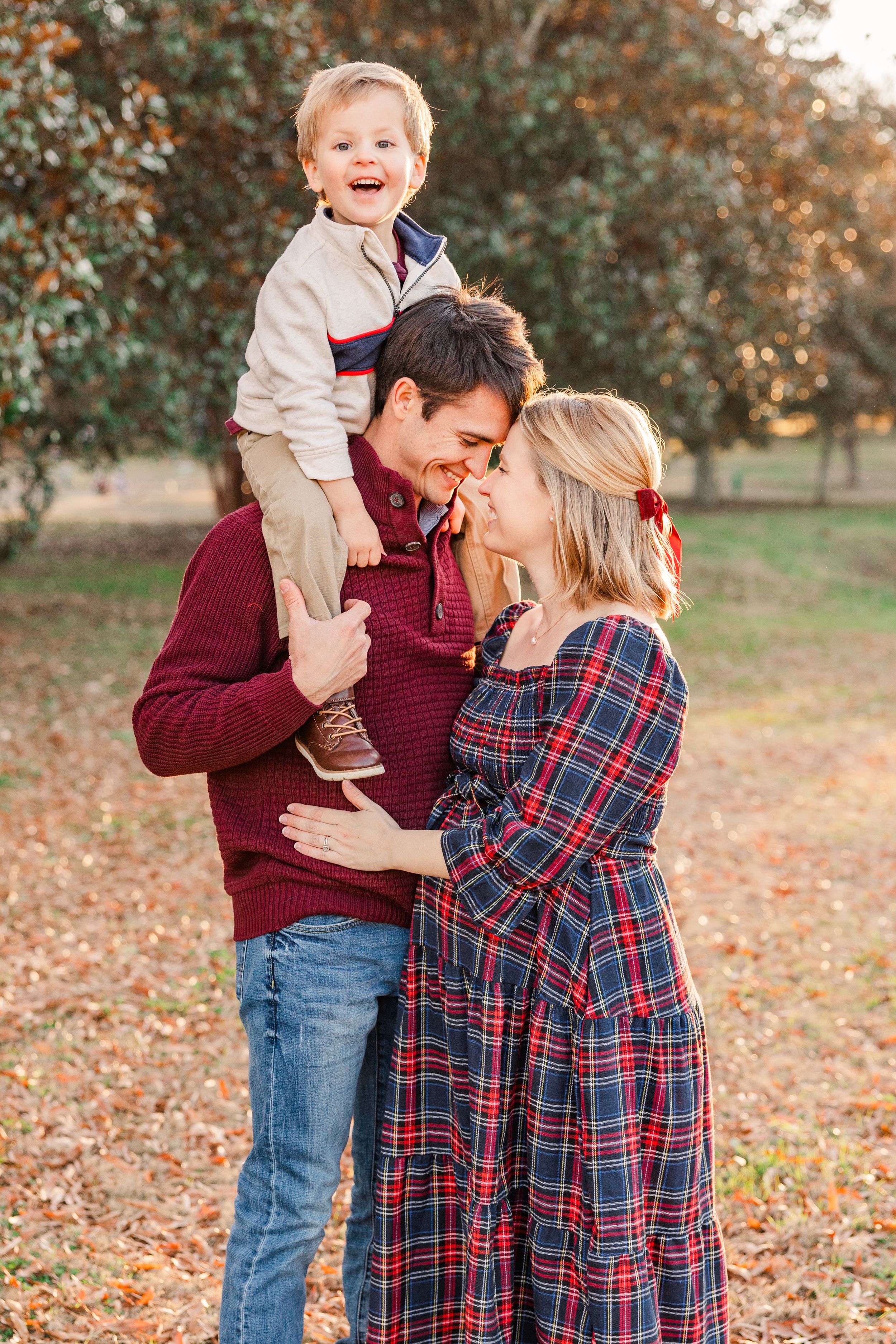 Family shares tender moment with child on father's shoulders and mother cradling baby bump.