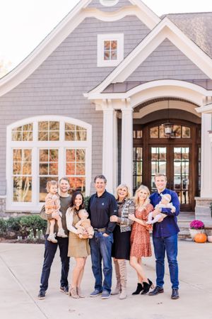 Extended family gathering outside large grey house with white trim and arched doorway.