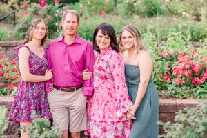 Group portrait of four people in pink and blue outfits standing in rose garden.