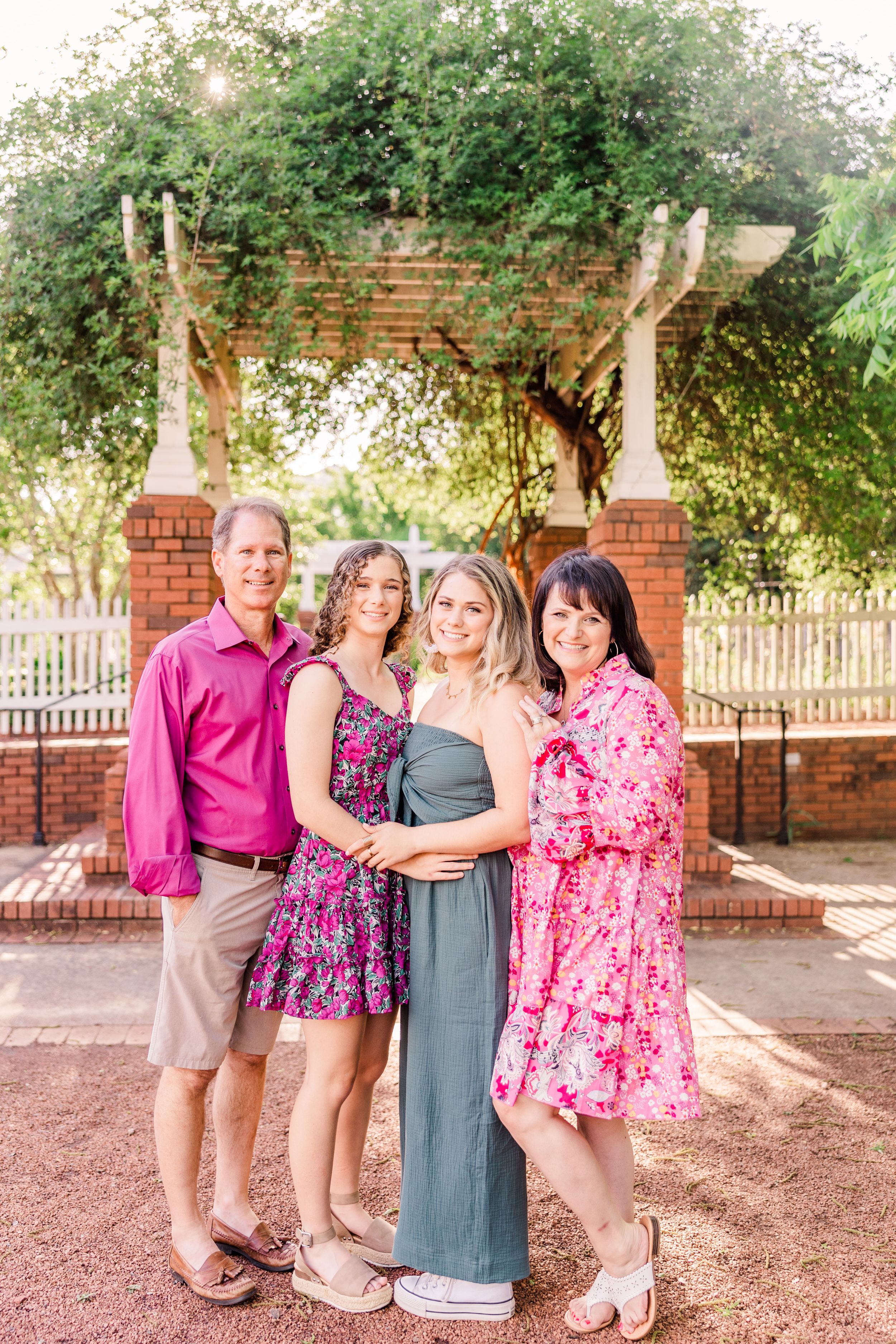 Family group portrait under garden pergola with brick columns and greenery.