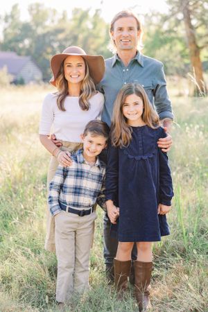 Family of four in coordinated casual outfits poses together in sunlit field.