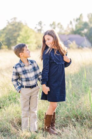 Young boy and girl in coordinated outfits stand together in late afternoon sunlit field.