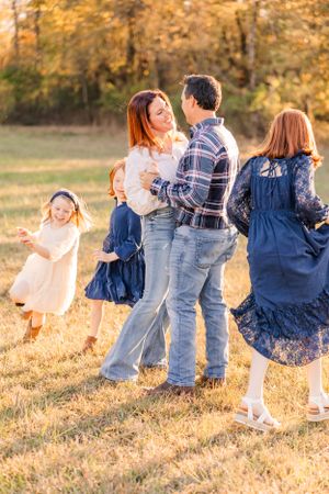 Family dances and spins together in a golden field during sunset photoshoot.