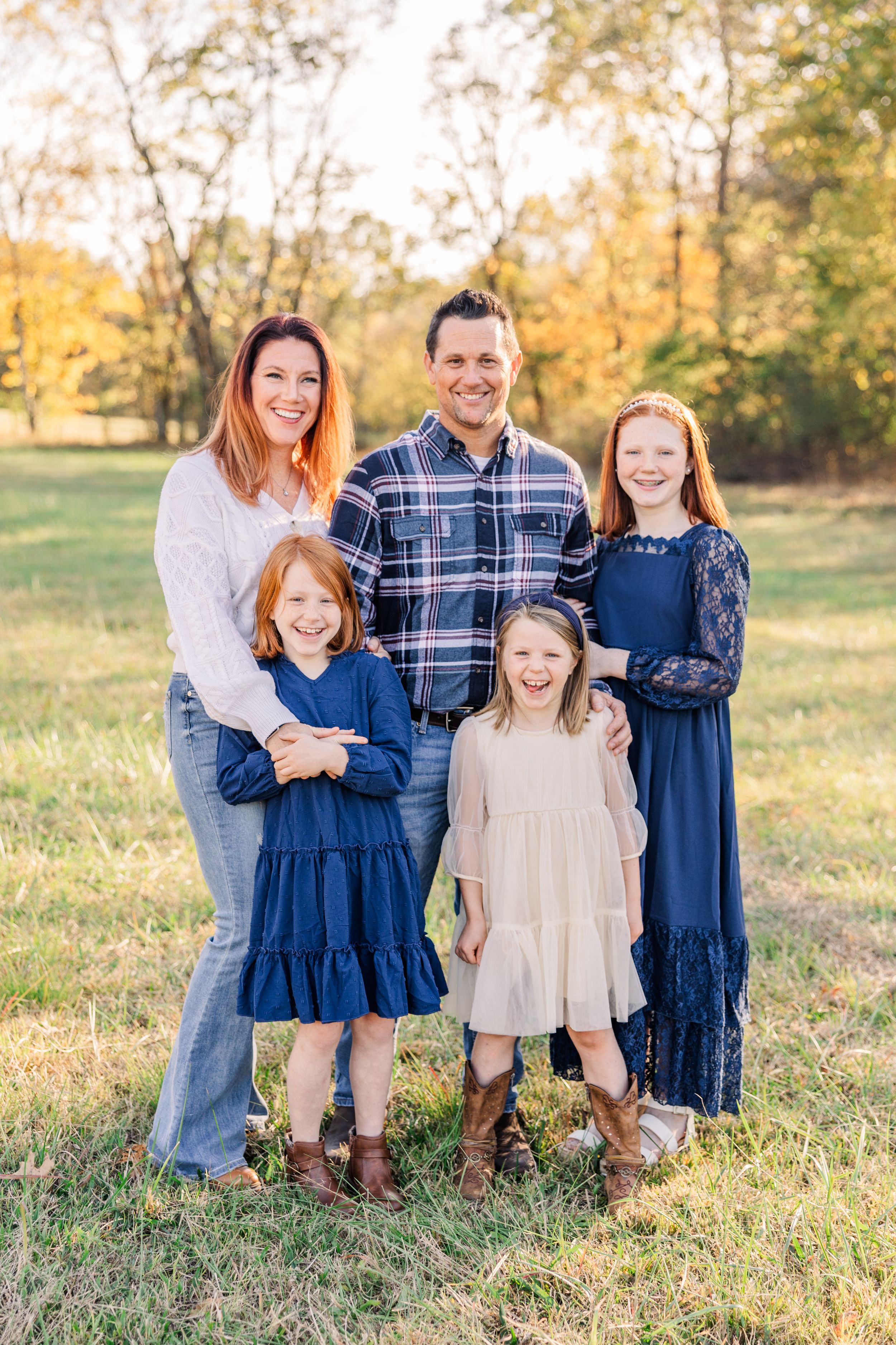 Family of five wearing coordinated navy and neutral outfits poses together in an autumn field at sunset.