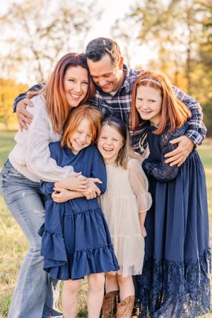Happy family embraces and laughs together during outdoor photoshoot in golden autumn light.