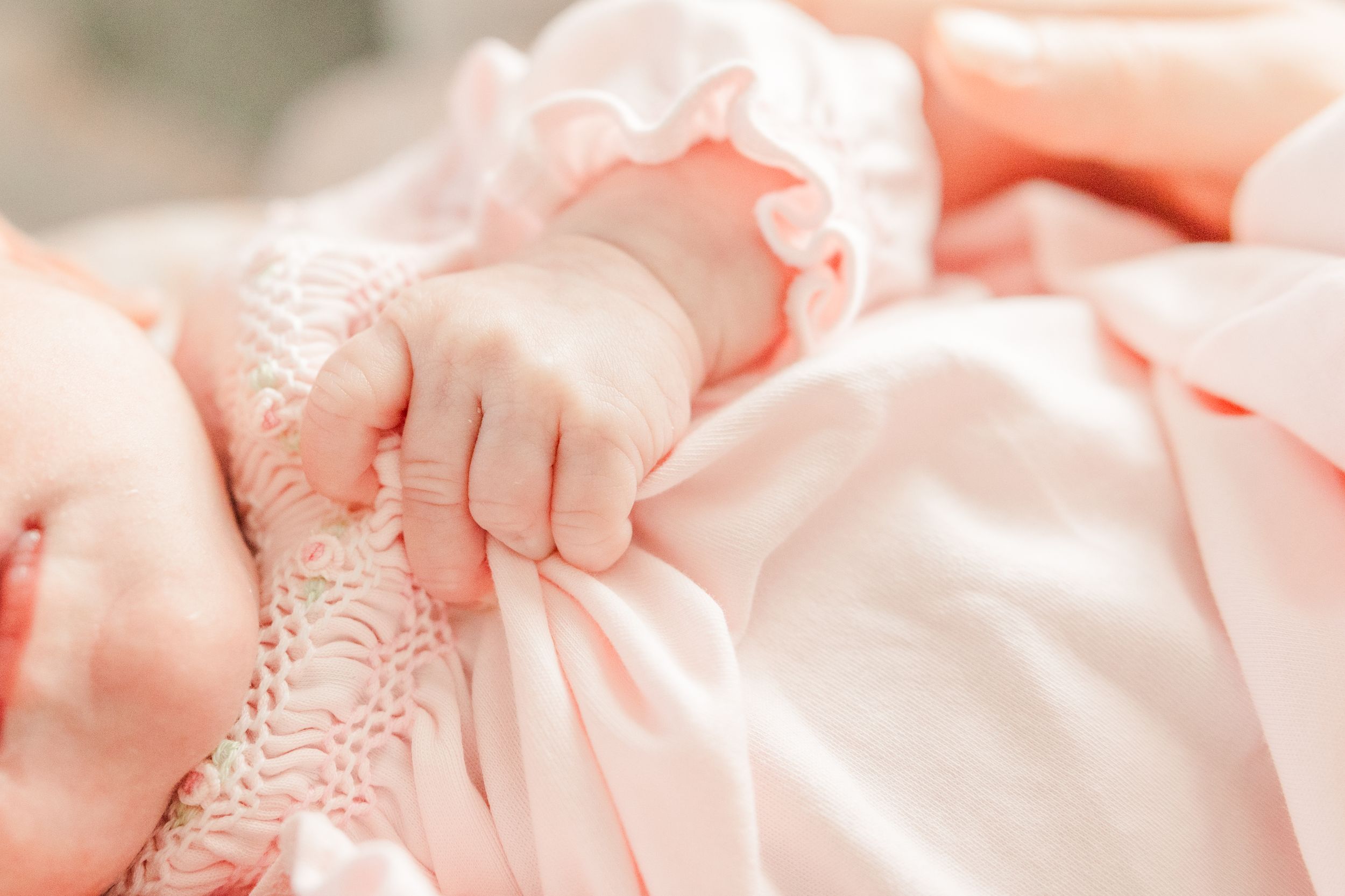 Close-up of baby's tiny hand grasping pink fabric during newborn photoshoot.