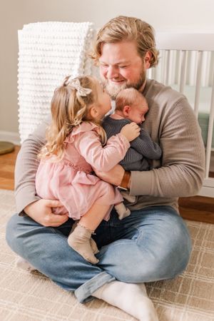 Family moment with toddler in pink dress cuddling with baby on floor.