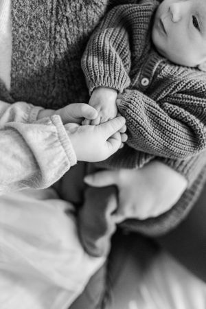 Close up black and white photo of adult hand holding tiny baby fingers.