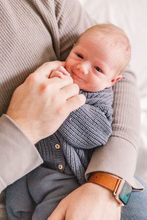 Baby in gray sweater smiling while being held.