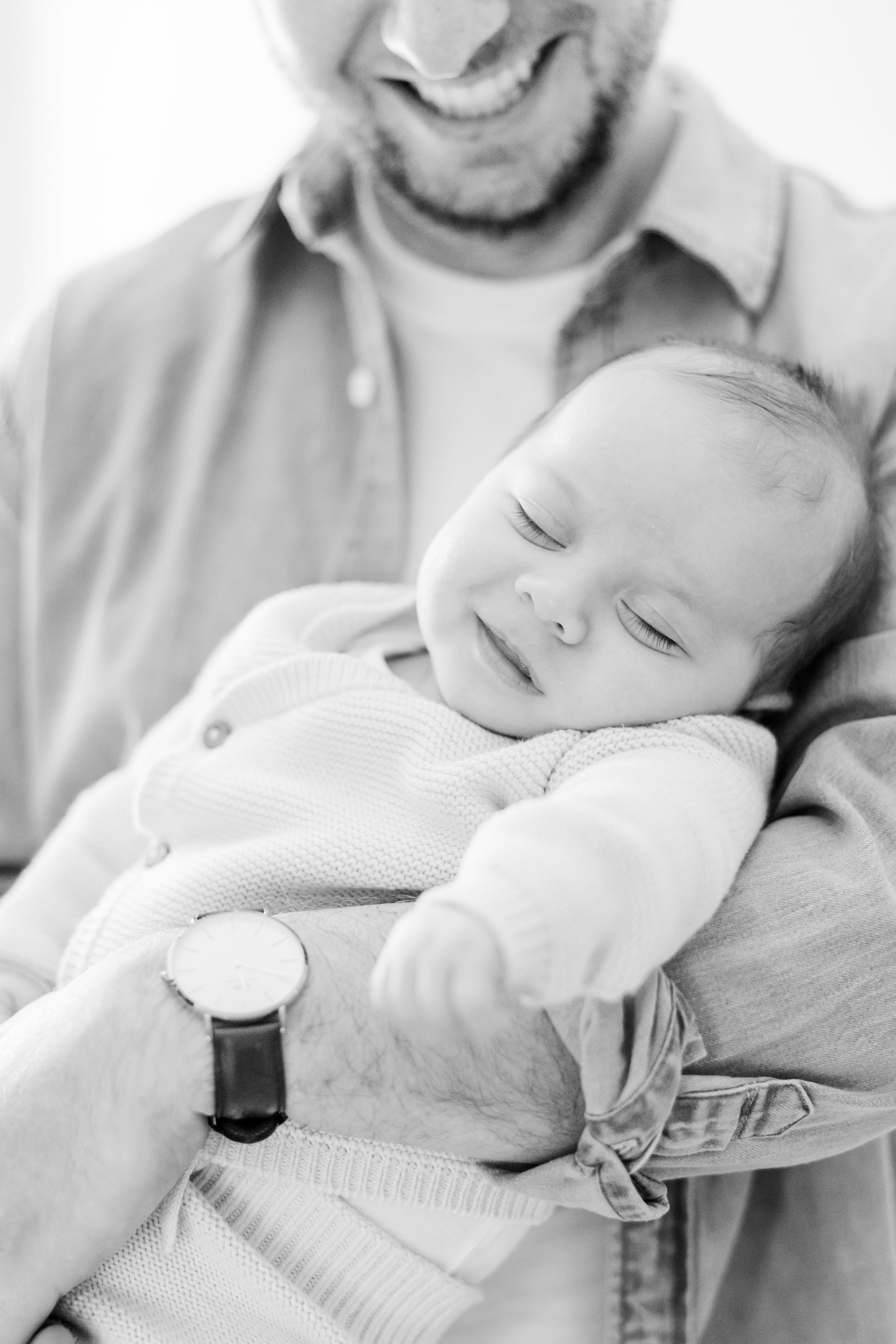 Black and white portrait of sleeping baby resting on parent's chest.