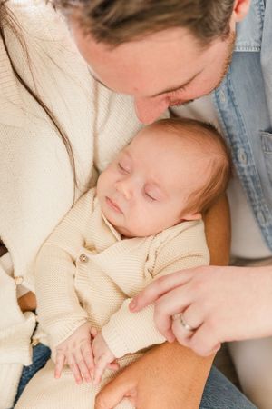 Parent gently kisses sleeping baby wearing cream knit sweater.