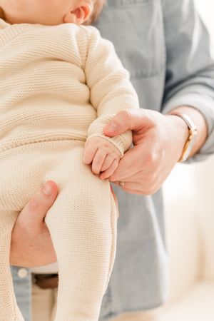 Close-up of hands holding an infant wearing a cream knit outfit.