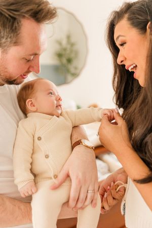 Family sharing joyful moment with baby wearing cream colored outfit in bright indoor setting.