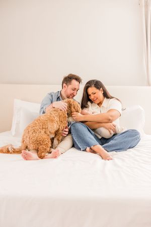 Couple relaxing on white bed with goldendoodle dog and newborn baby.