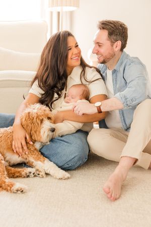 Family relaxes on couch with baby and golden doodle dog in bright living room.