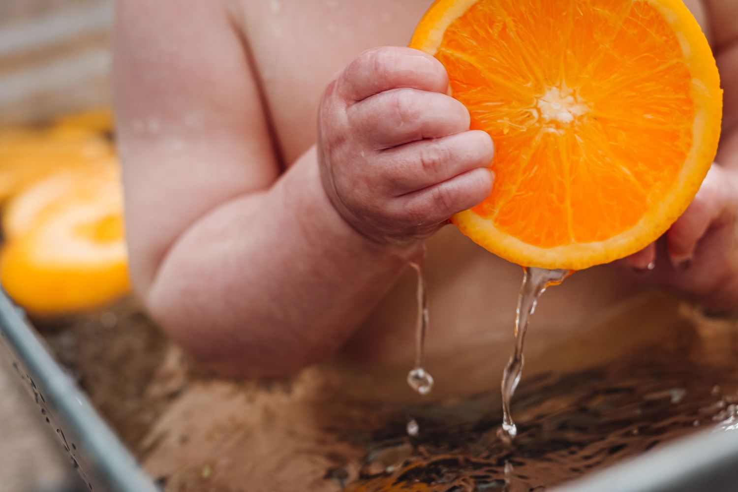 Small hands squeezing an orange half with juice dripping down. Fruit bath session