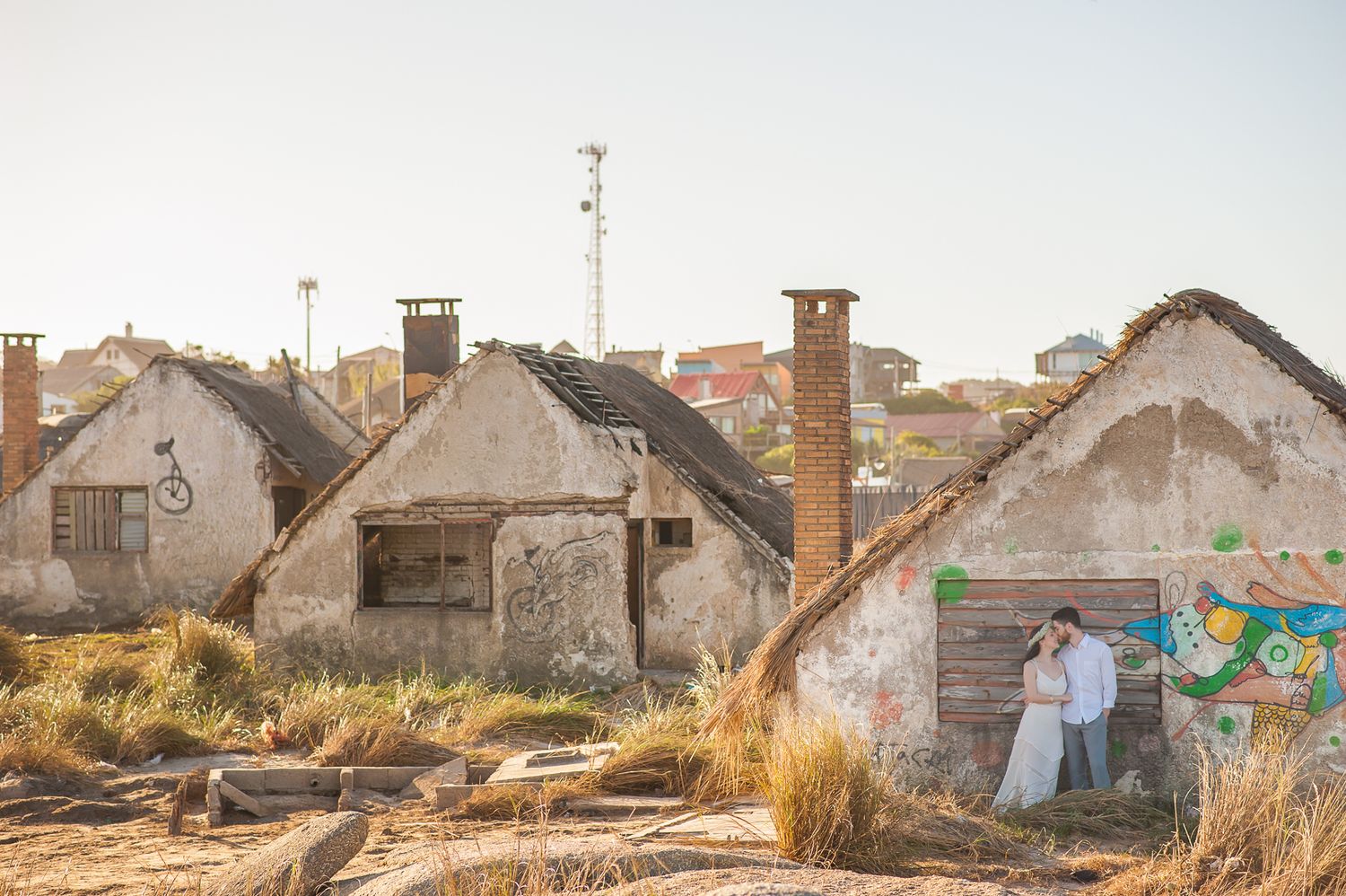 Golden hour light illuminates abandoned buildings as couple poses in urban decay setting.