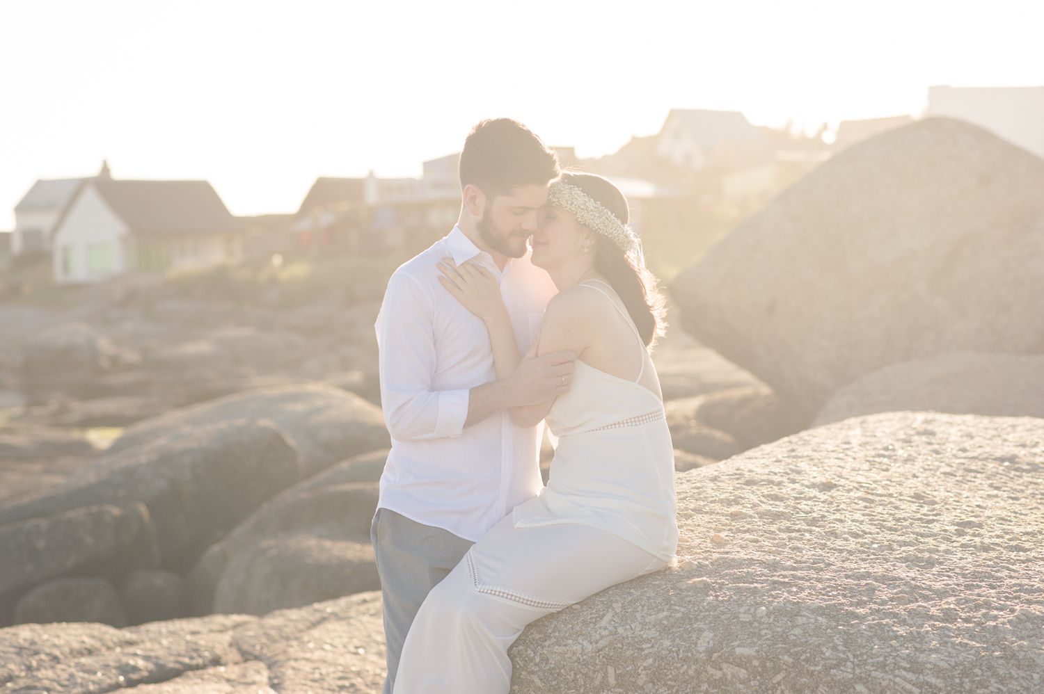 A couple sits together on coastal rocks during golden hour while wearing white.