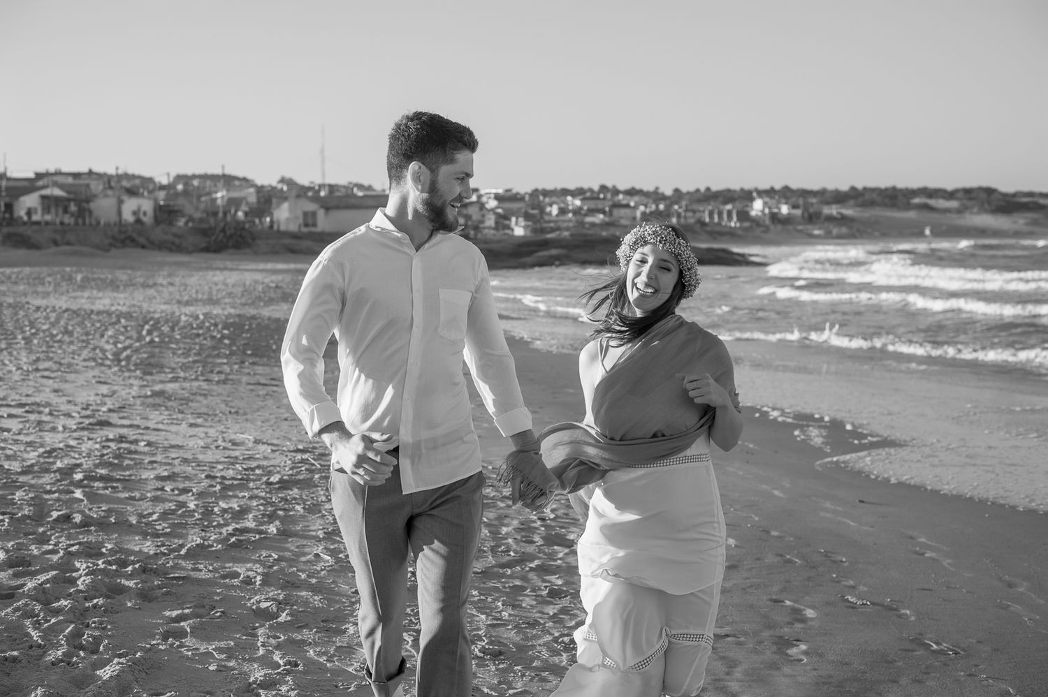 A couple walks together laughing along a windy beach shore.