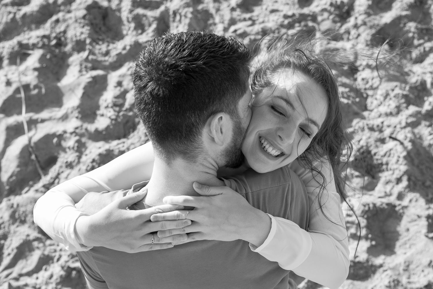 A joyful embrace captured in black and white against a textured stone wall.