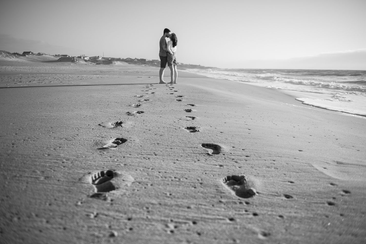 A romantic silhouette and footprints in the sand along an empty beach at sunset.