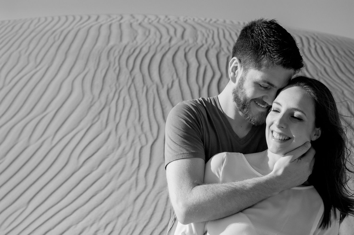 An intimate black and white portrait against rippling sand dunes.