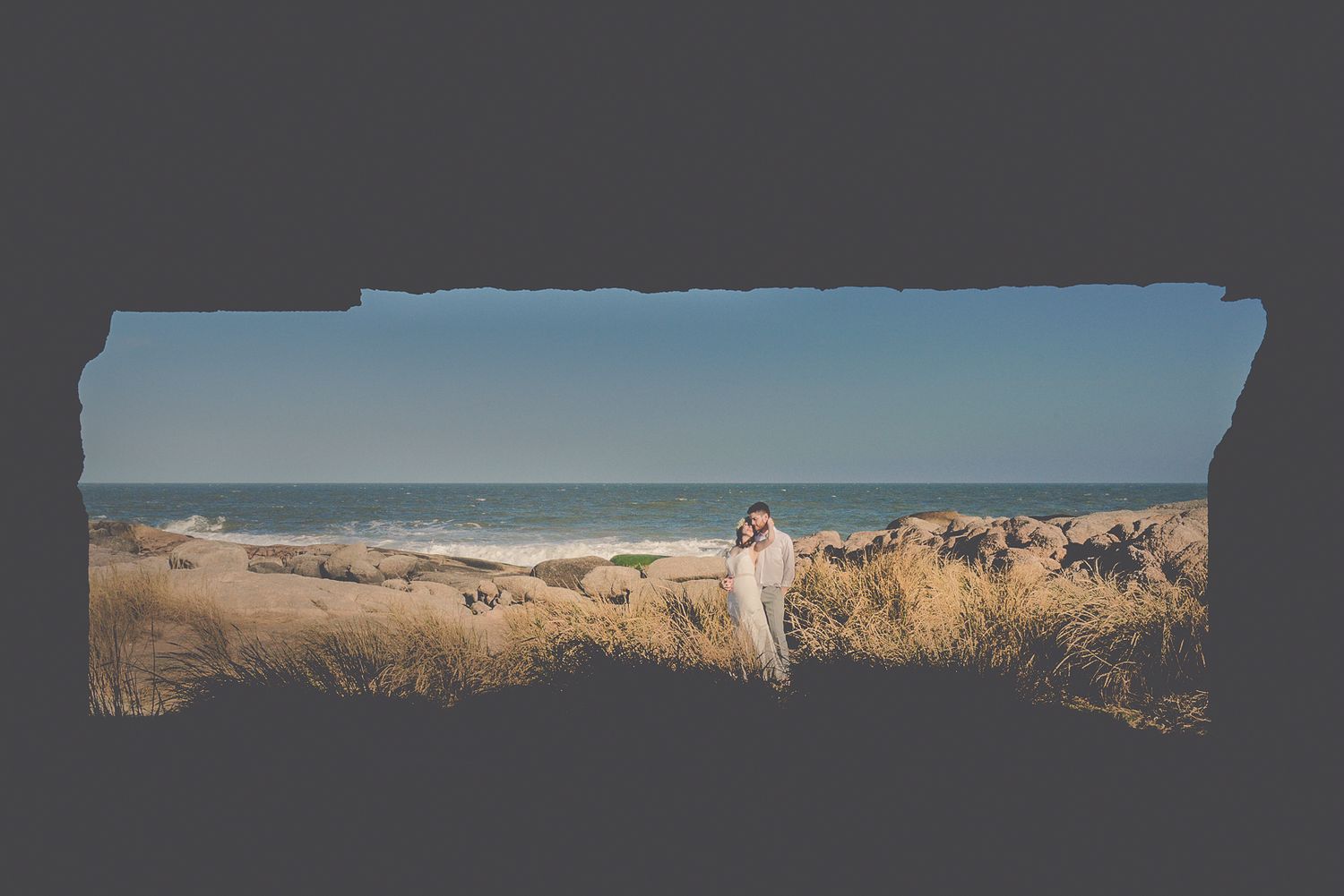 Panoramic beach scene with couple walking through sand dunes at sunset.