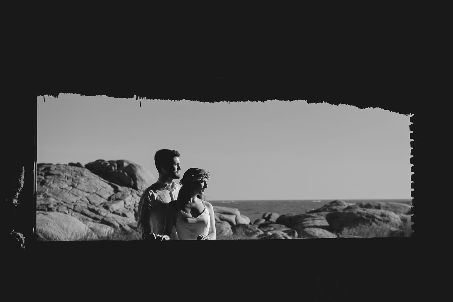 Artistic black and white panoramic shot of couple against rocky coastal landscape.