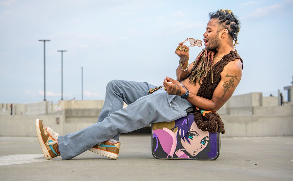 Casual seated pose on a skateboard in an empty parking lot with utility poles in the background at dusk.
