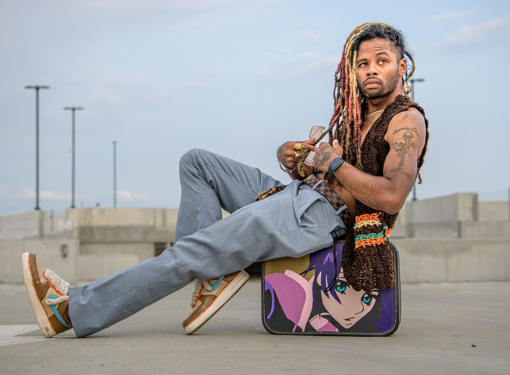 Casual seated pose on a skateboard in an empty parking lot with utility poles in the background at dusk.