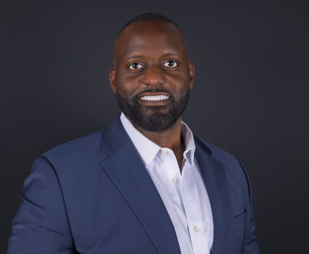Professional headshot series of a person in a navy suit and white shirt against dark background showing various expressions.