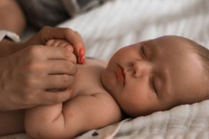 Close-up of gentle hands massaging a baby's belly on white bedding.