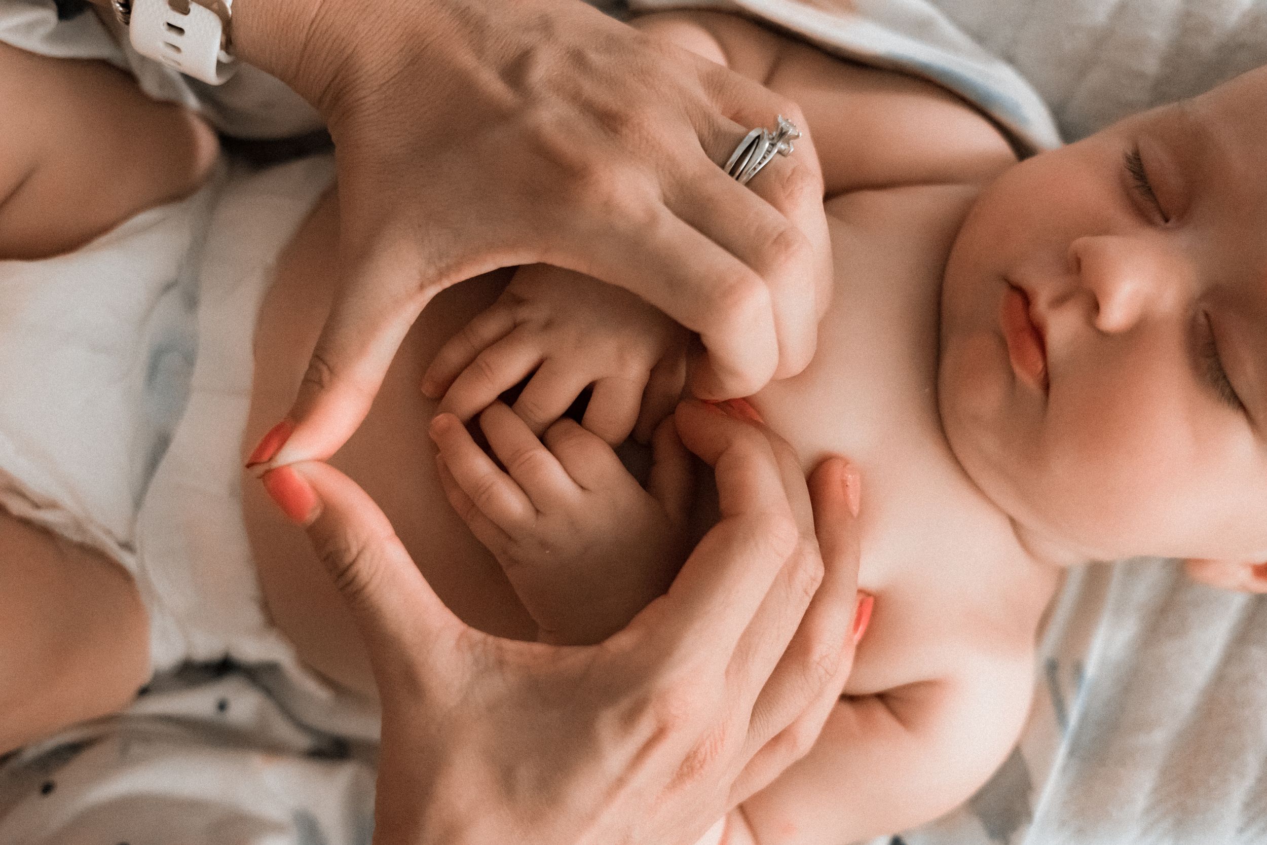 Tender massage of baby's chest and torso on soft white sheets.