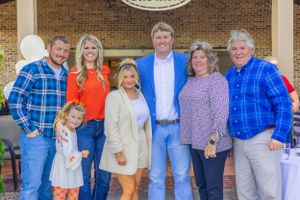 Group of people in casual attire gathered for a celebratory photo against brick wall backdrop.