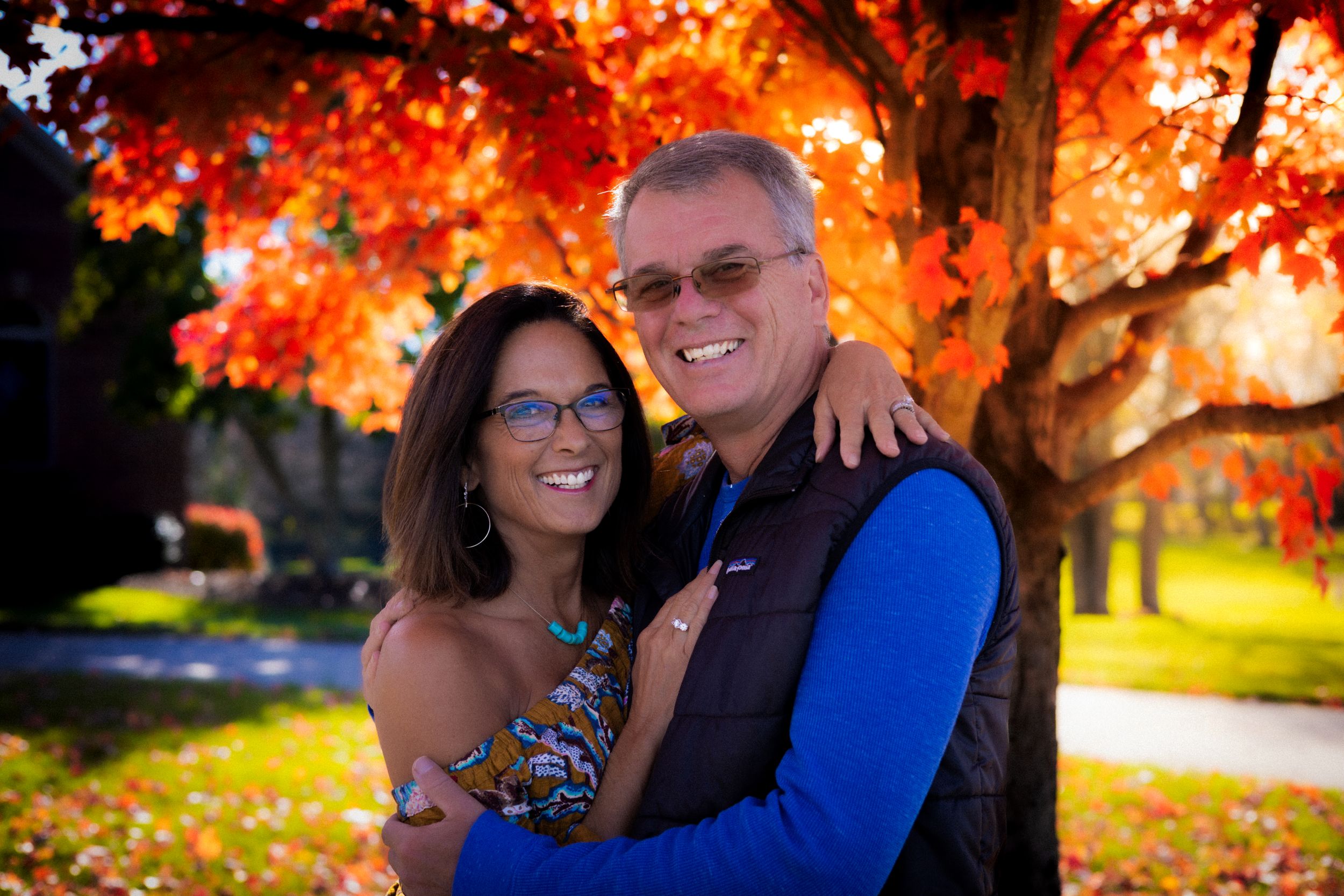 Couple poses together in front of vibrant autumn foliage with orange maple leaves.