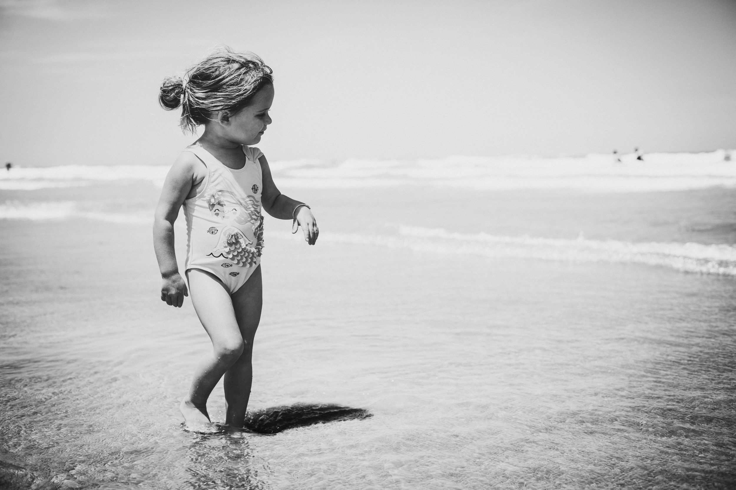 Black and white photo of child playing in shallow ocean waves.