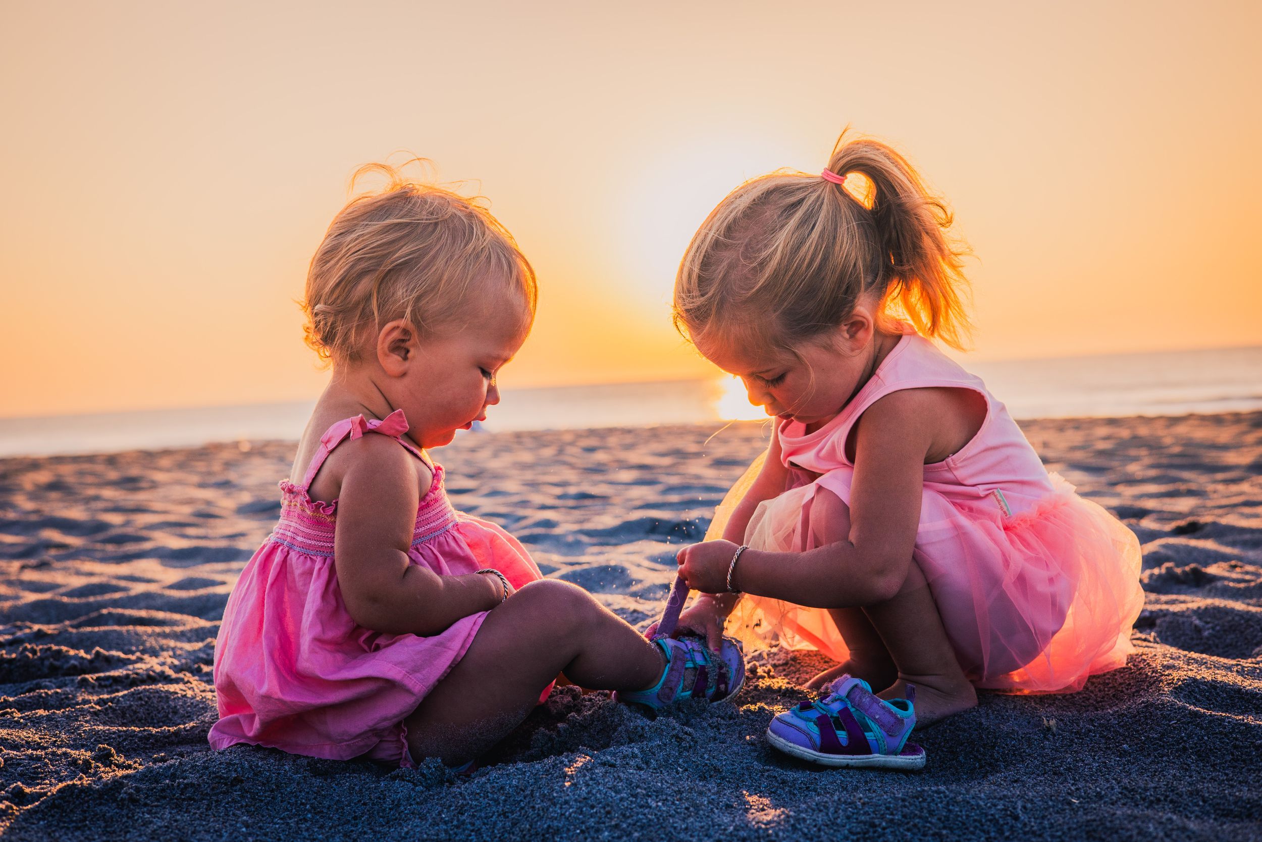 Children in pink swimwear playing together on beach sand during golden hour.