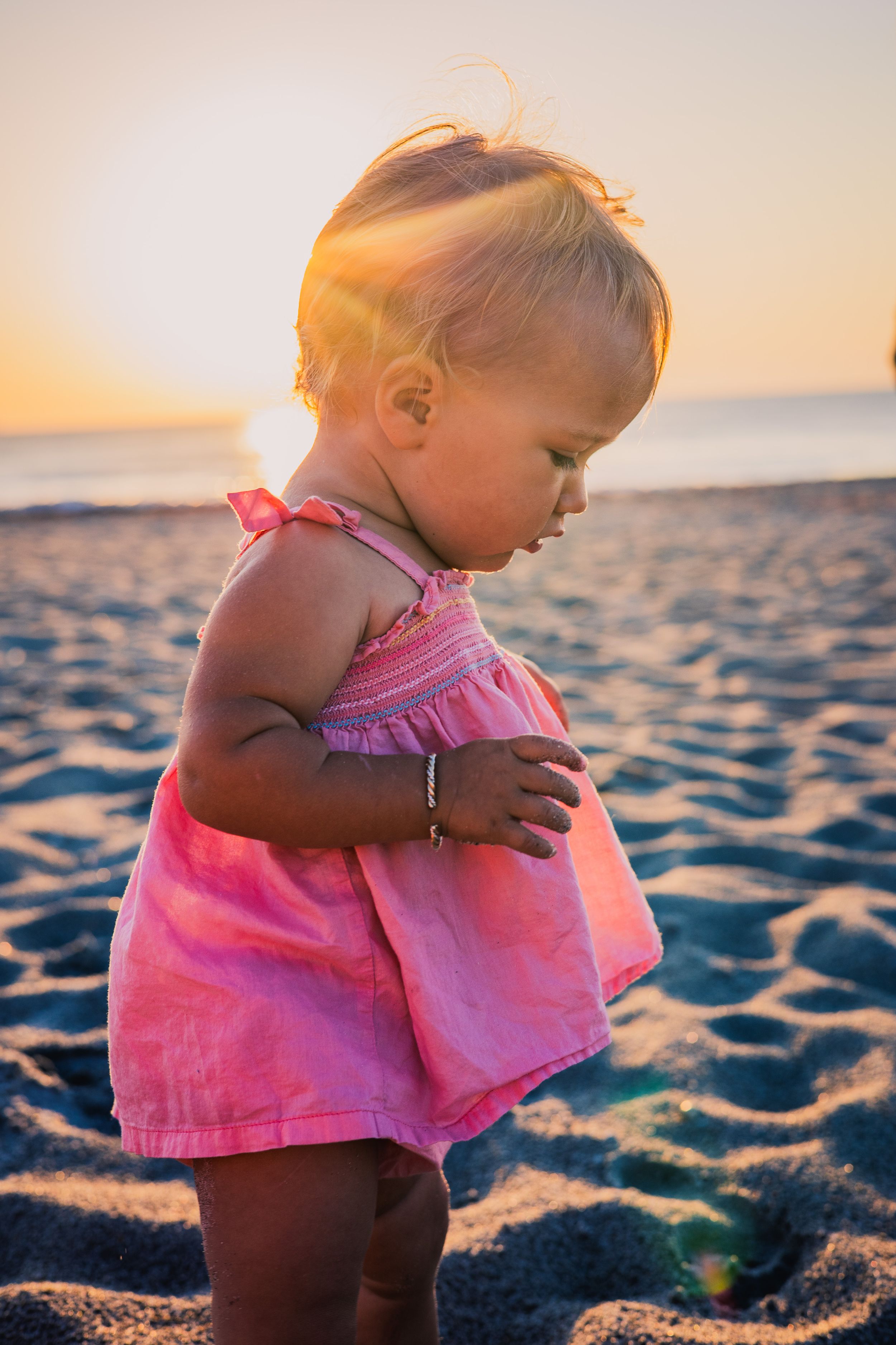 Small child playing in pink outfit at sunset on sandy beach.