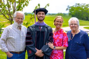 Family gathering outdoors for graduation photos with person in cap and gown.