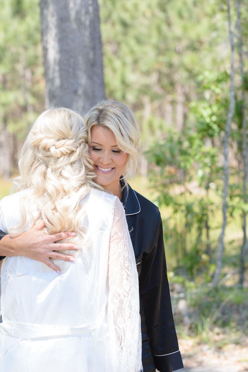 Wedding party members share a heartfelt embrace on a bright sunny day against a natural outdoor background.
