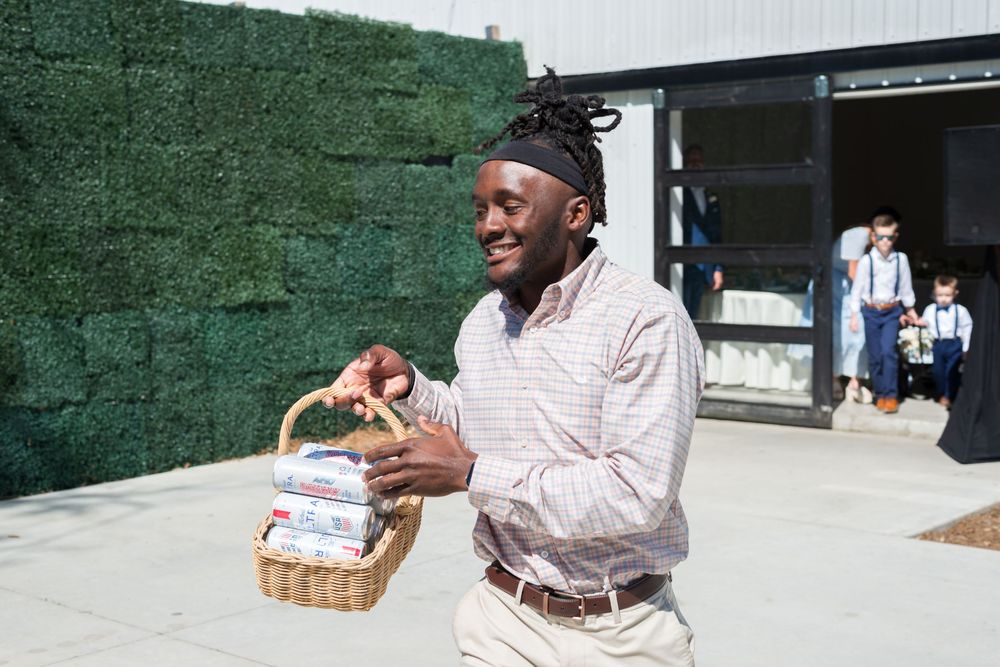 Person in light colored shirt carrying a woven basket while walking past a green wall on a sunny day.