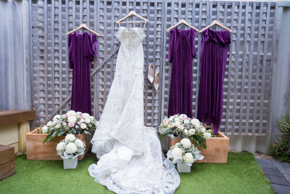 Wedding dresses displayed with purple bridesmaid gowns against a textured wall with floral decorations.