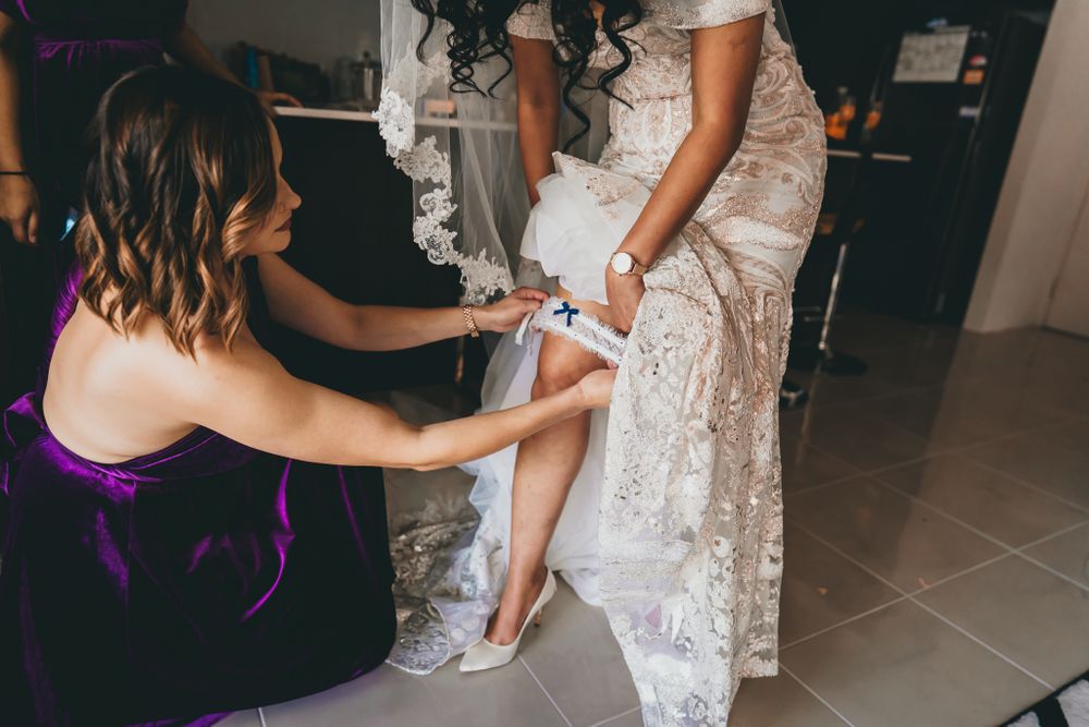 Helper assisting with putting on elegant white lace wedding shoes during bridal preparations.
