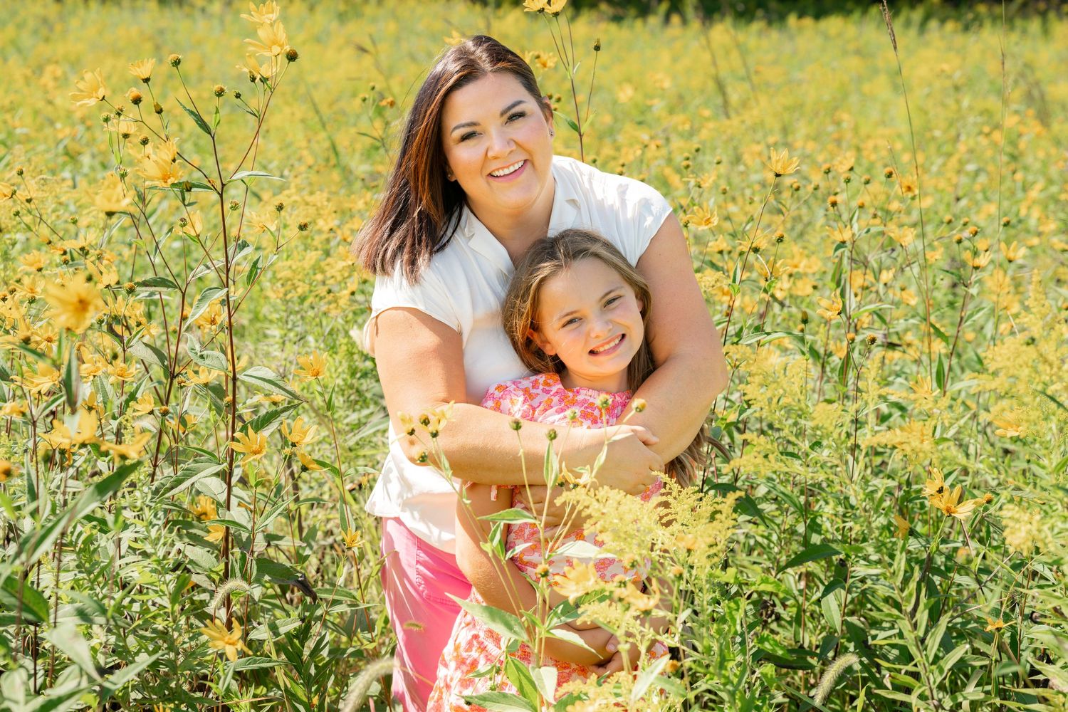 A joyful outdoor portrait of people embracing in a field of bright yellow wildflowers on a sunny day.