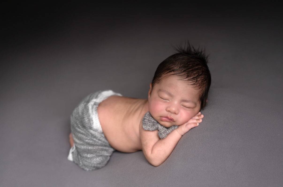 Sleeping newborn baby boy wearing gray wrap and bow tie on a gray background. Embracing Life’s Beauty