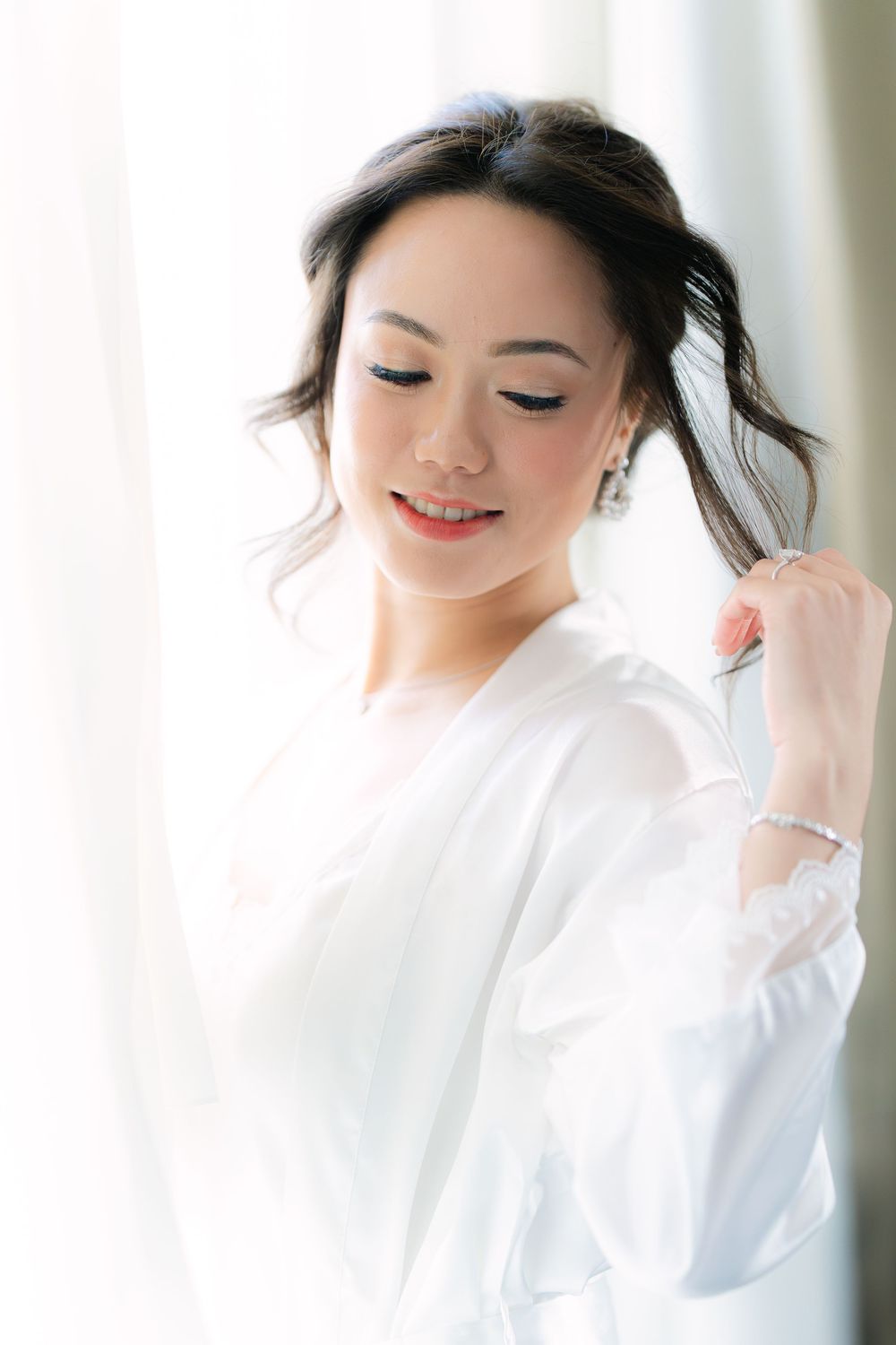 bride in a white robe adjusting her hair during wedding morning preparations